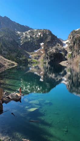 Vertical-4k,-Young-Woman-in-Bikini-Walking-on-Rocks-by-Beautiful-Alpine-Lake-With-Mirror-Reflection-of-Mountain-Hills