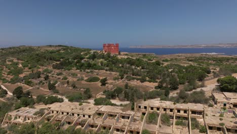 Hotel-De-Festival-Abandonado-En-Ruinas-Antiguas-Con-La-Torre-Roja-Al-Fondo-En-La-Bahía-De-Mellieha,-Malta