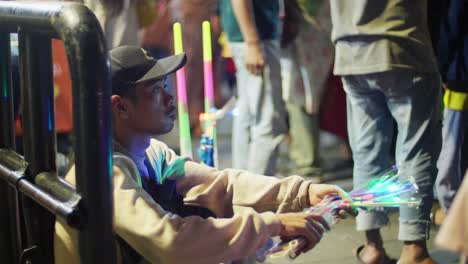 Un-Vendedor-Ambulante-Vende-Juguetes-Brillantes-En-Taman-Fatahillah-En-Yakarta,-Rodeado-Por-Un-Concurrido-Mercado-Nocturno.