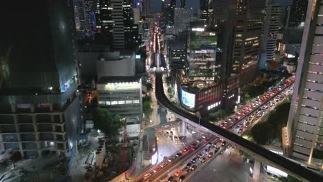 Drone-establishing-of-Thai's-business-hub,-Bangkok-modern-buildings-at-night,-illuminated-car-traffic-jam