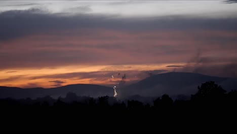 Fireworks-sparkle-and-shimmer-fading-away-at-dusk-with-mountain-silhouette,-slow-motion