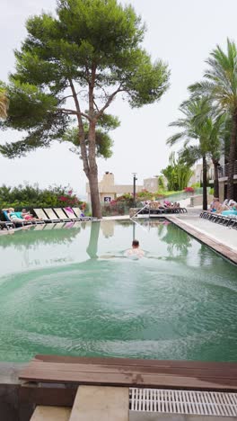 Vertical-shot-of-male-tourist-jump-in-beach-hotel-pool-head-first,-Mallorca