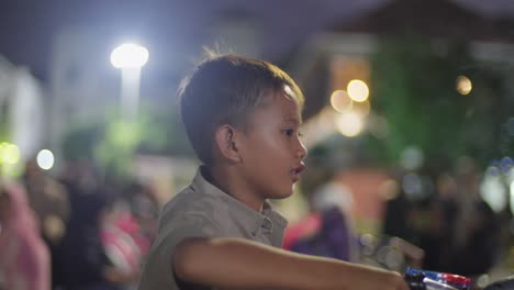 A-boy-riding-a-bike-at-night-in-a-bustling-Taman-Fatahillah,-Jakarta