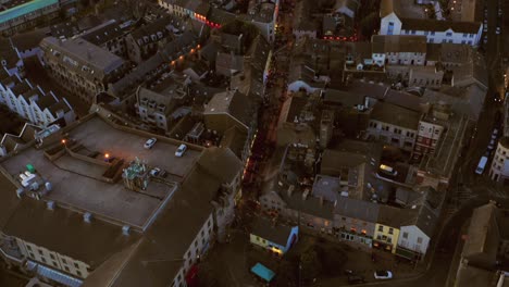 Aerial-tilt-down-view-of-Galway-city-center-at-night-during-the-Arts-Festival,-showcasing-illuminated-streets-and-festival-activities