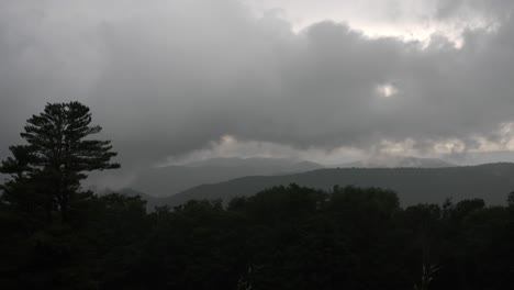 Dark-clouds-move-slowly-across-a-gloomy-sky,-casting-shadows-over-a-forested-mountain-landscape