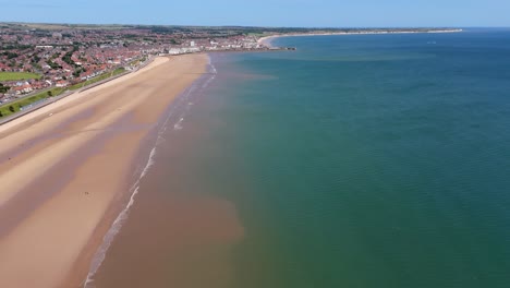 Imágenes-Aéreas-Sobre-La-Playa-De-Fraisthorp-Con-Bridlington-Al-Fondo-En-Verano-En-Un-Día-Caluroso-Y-Soleado,-Cielo-Azul-Y-Agua-Azul