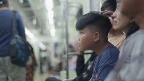 Un-Niño-Parece-Pensativo-Mientras-Viaja-En-Un-Tren-Lleno-De-Gente-En-La-Ciudad