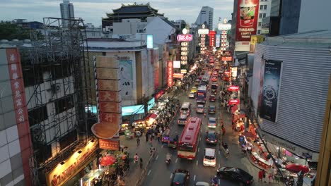 Drone-fly-busy-Chinatown-streets-of-Bangkok,-Thailand-at-early-nighttime,-neon-sign-and-street-food-stalls-vendor