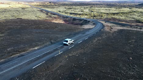 Ein-Auto-Auf-Einer-Kurvenreichen-Straße-Im-Isländischen-Hochland,-Vorbei-An-Moosfeldern-Und-Hügeln,-Erreicht-Eine-Weite-Ebene