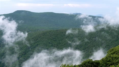 Static-handheld-shot-captures-clouds-gliding-lower-left-to-right,-enveloping-forested-mountain-peaks