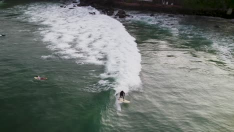 Surfers-riding-waves-off-the-coast-of-Sri-Lanka-at-sunset,-aerial-view