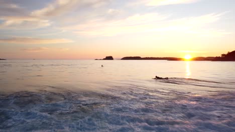 Surfers-ride-waves-at-sunset-in-Tofino-on-Vancouver-Island-with-stunning-coastline-views