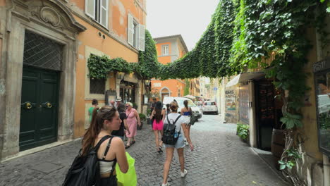 Tourists-and-visitors-roam-the-side-streets-of-Trastevere-on-a-beautiful-sunny-day-walking-over-historic-brick-streets-below-vibrant-buildings