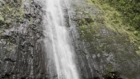 A-stunning-waterfall-cascading-down-a-rocky-cliff-surrounded-by-vibrant,-lush-greenery-in-Oahu