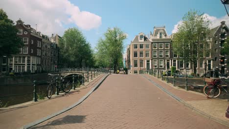 Floating-through-Amsterdam-historic-cityscape-with-canal,-landmark-houses,-and-bridges