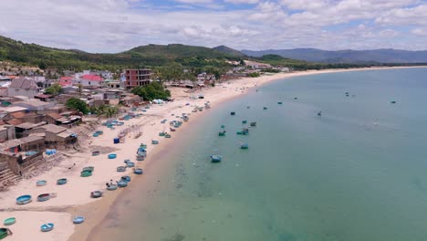 Coracle,-Botes-De-Cesta-En-La-Costa-Y-Barcos-De-Pesca-Sobrevuelan-La-Costa-Arenosa-Y-Las-Aguas-Del-Mar-Azul-Verde-Agua-Del-Pueblo-Pesquero,-Vietnam