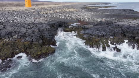 Un-Vídeo-Impresionante-Muestra-Un-Faro-Naranja-En-La-Escarpada-Costa-De-Islandia,-Rodeado-De-Vastos-Paisajes-Y-Olas-Rompiendo-Contra-Costas-Rocosas.