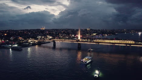 Side-view-of-the-golden-horn-bridge-with-metro-at-night,-blue-hour-in-Istanbul-with-stunning-lights-and-boats,-copy-space-and-slow-motion