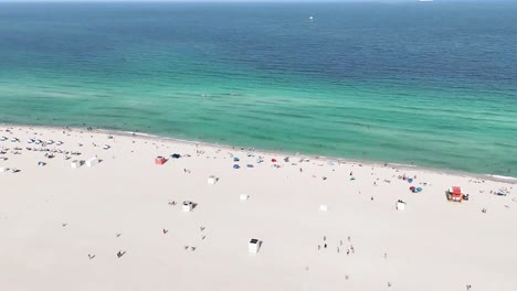 Die-Drohne-Steigt-In-Einer-Wirbelnden-Bewegung-Auf,-Beginnend-Mit-Dem-Strand-Und-Dem-Meer,-Zeigt-Ein-Kreuzfahrtschiff,-Das-Den-Hafen-Verlässt,-Und-Dreht-Sich,-Um-Gebäude-Und-Häuser-In-South-Beach-Freizugeben