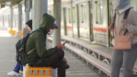 Passengers-waiting-for-the-train,-heads-down,-absorbed-in-their-phones-in-Kampung-Bandan-electric-train-station