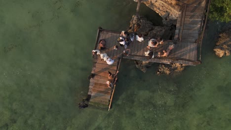 Top-down-aerial-descending-view-pier-of-The-Rock-Restaurant-with-tourists-waiting-for-a-shuttle-boat-on-the-sunset