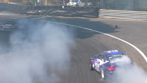 Race-cars-drifting-and-burning-tires-with-lots-of-smoke-on-a-tight-curve-followed-by-a-drone