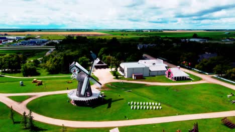 Mennonite-Heritage-Village-aerial-flyover-sunny-summer-day-as-wedding-planner-team-setup-white-chair-in-10-rows-with-2-isles-on-a-lush-green-grass-lawn-next-to-historic-windmill-180-degree-panoramic