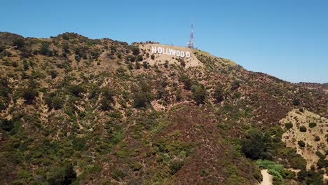 Toma-Aérea-De-Establecimiento-Del-Cartel-De-Hollywood-En-Beverly-Hill-Contra-El-Cielo-Azul-Con-Torre-De-Transmisión-En-EE.UU.