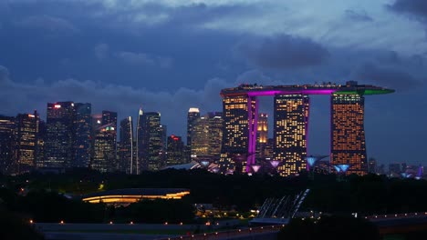 Dusk-to-night-time-lapse-shot-at-marina-barrage-rooftop-park-overlooking-at-Supertree-grove-in-Gardens-by-the-bay-and-downtown-cityscape-featuring-landmark-Marina-Bay-Sands-against-fast-moving-clouds