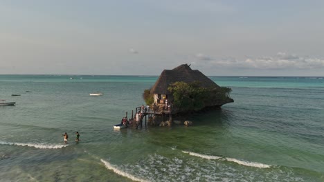 Tourists-embark-on-wooden-pier-of-The-rock-Restaurant-during-high-tide,-Zanzibar,-Tanzania