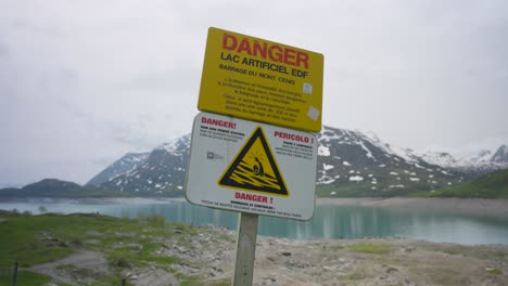 A-danger-sign-in-front-of-a-scenic-alpine-lake-warns-of-danger-at-dam