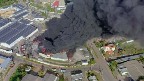 Drohnenaufnahmen-Des-Fabrikinfernos-–-Zoom-Out-Ansicht-Zeigt-Dichten-Rauch-Und-Verheerende-Flammen,-Die-Das-Karibische-Gebäude-Verwüsten