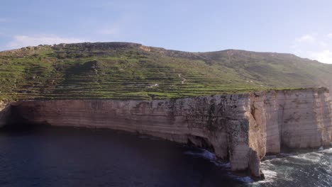 Drone-footage-of-very-tall-cliffs-by-the-sea,-with-lush-greenery-atop-the-cliffs-in-Malta