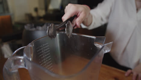 Hermosa-Toma-En-Cámara-Lenta-De-Una-Joven-Barrendera-Recogiendo-Un-Cubo-De-Hielo-Con-Pinzas-Para-Preparar-Un-Cóctel-En-La-Barra-De-Un-Bar-Restaurante.