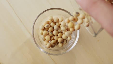 Overhead-View-Of-Soybean-Pods-Slowly-Pouring-In-Clear-Glass-Jar