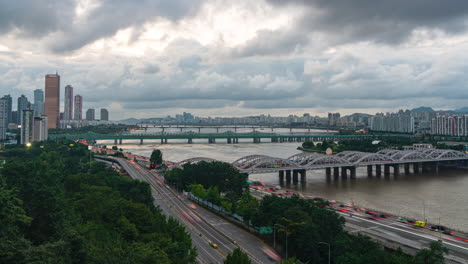 Seoul-Yeouido-Urban-Skyline-at-Sunset-with-fast-clouds-Movement,-Busy-Car-Traffic-on-Olympic-daero-Highway,-View-of-Han-River-and-Hangang-Railway-Bridges---Day-to-Night-Timelapse