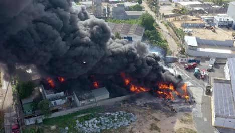 Stunning-aerial-drone-shot-of-a-factory-on-fire-in-the-Caribbean,-showing-thick-black-smoke-rising-into-the-sky