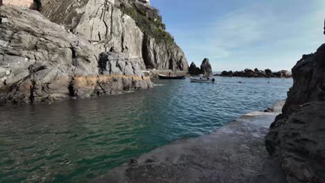 Tourist-boats-floating-near-the-rocky-and-rugged-coastal-scenery-of-Manarola,-Italy,-capturing-the-essence-of-seaside-adventure-and-natural-beauty