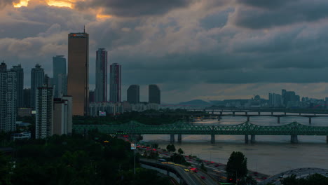 Sonnenuntergang-In-Seoul-Mit-Dramatischer-Wolkenbewegung-über-Der-Skyline-Der-Stadt,-Wolkenkratzer-Im-Stadtteil-Yeouido,-Zeitraffer-Des-Autoverkehrs-Und-Der-Hangang-Eisenbahnbrücke---Hochwinkelansicht