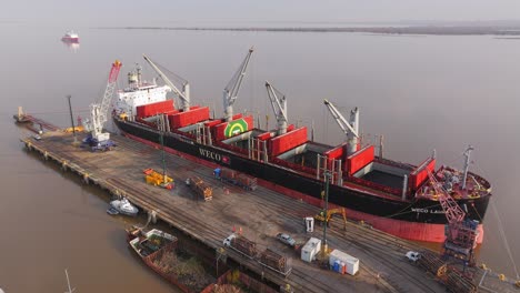 Cargo-ship-Weco-Laura-along-Uruguay-river-loading-logs-with-cranes-and-excavators