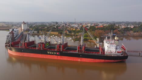 Cargo-ship-Weco-Laura-along-Uruguay-river-loading-logs-with-cranes-and-excavators