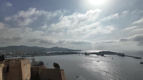 Zeitraffer-Der-Burg-Und-Der-Stadt-Ibiza-Mit-Einem-Sich-Ständig-Verändernden-Bewölkten-Himmel-Und-Yachten,-Die-In-Der-Hauptverkehrszeit-Am-Frühen-Morgen-Abfahren