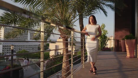 Young-female-wear-long-white-dress-and-stand-near-beach-hotel-balcony,-Spain