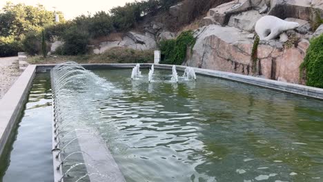 Pull-out-on-fountains-reveals-a-blonde-woman-in-an-orange-dress-sitting-by-the-fountain-and-reading-a-book