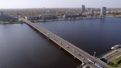 Aerial-view-of-a-trafficked-bridge-above-a-lake-with-Riga's-cityscape-in-the-background