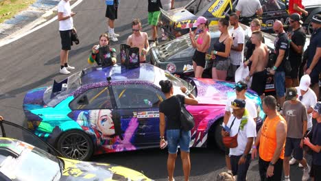 Race-cars-exhibition-on-the-racing-tracks,-people-checking-on-the-race-car-and-female-pilot-handing-gifts-and-getting-picture-taken