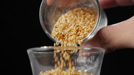 Korean-Sesame-Seeds-Are-Poured-Into-A-Glass-Jar-With-A-Black-Backdrop