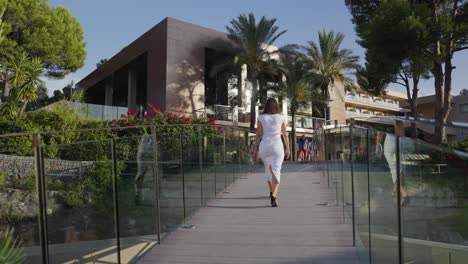 Woman-in-white-long-dress-walk-on-exotic-beach-hotel-bridge,-Mallorca