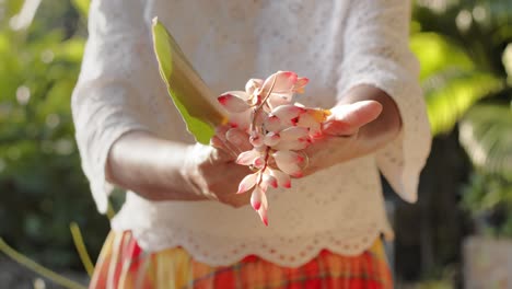 Woman-in-white-shirt-and-plaid-skirt-showing-Alpinia-zerumbet-flower-to-camera