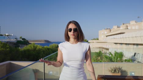 Mujer-Elegante-Con-Gafas-De-Sol-Y-Vestido-Caminando-Por-El-Balcón-De-Un-Hotel-De-Playa,-Mallorca